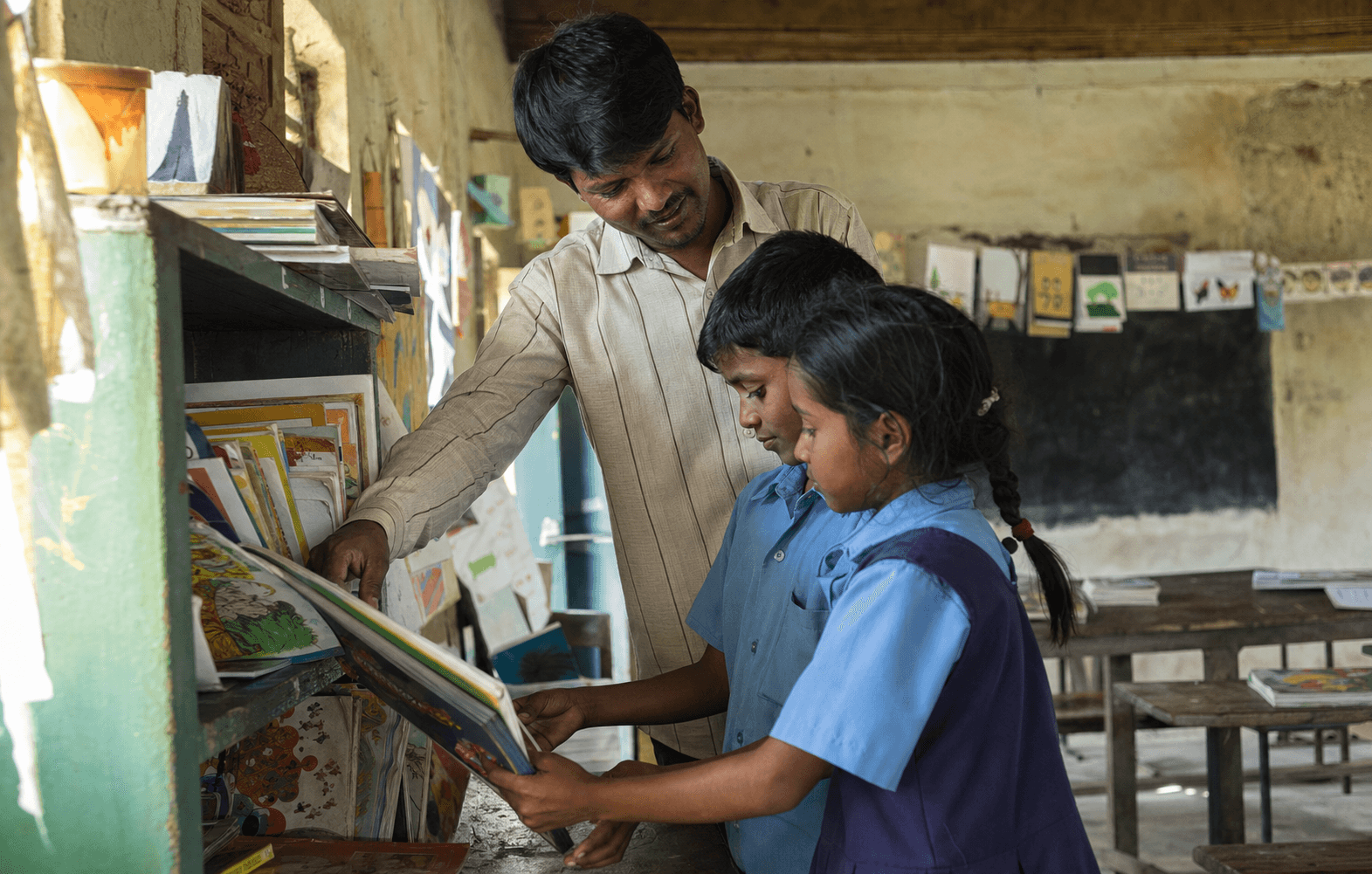 Teacher helping two students choose books from a rural classroom library